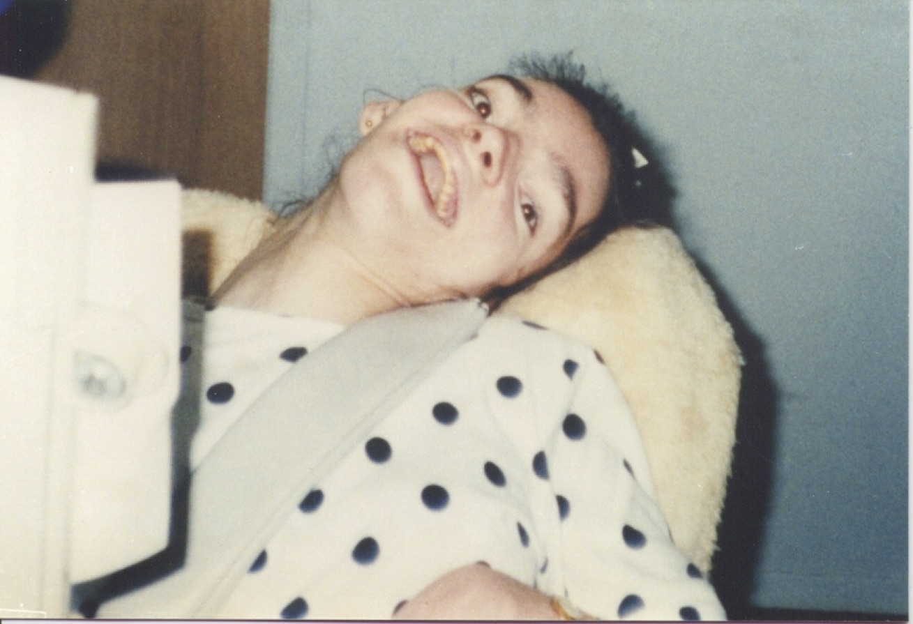 A close-up view of a young woman with dark hair and brown eyes sitting in a chair and smiling with her head tipped back.